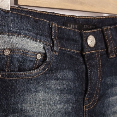 Pormenor de jeans de ganga escura pendurado num cabide de madeira