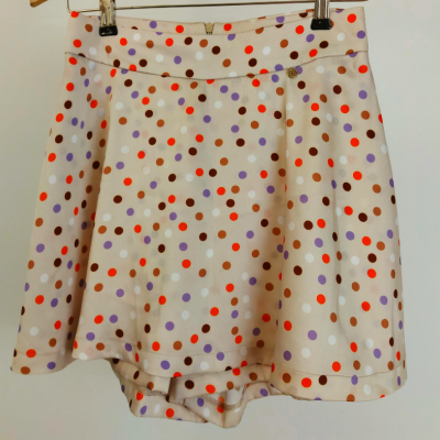 Saia-calção bege com bolinhas coloridas pendurada num cabide