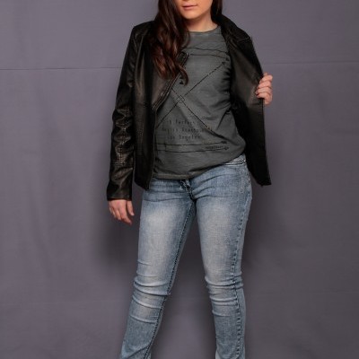 Jovem com casaco preto, camisola cinza com texto e calças de ganga azuis