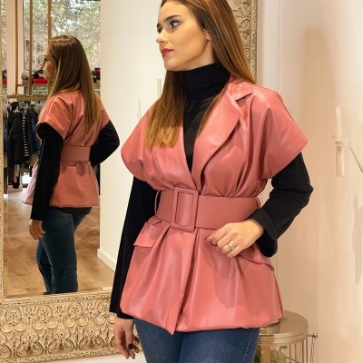 Colete feminino rosa acetinado com cinto largo sobre camisola preta de gola alta e jeans azuis