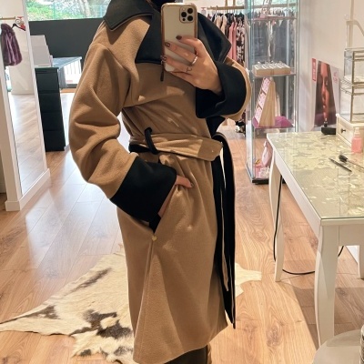 Mulher a usar sobretudo bege com detalhes pretos a tirar selfie num interior