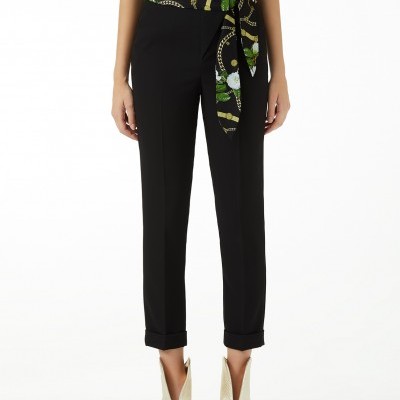 Calças pretas com bainha dobrada e blusa estampada com correntes e flores.