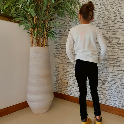 Criança de costas com roupa casual e vaso alto com plantas em fundo de parede decorativa