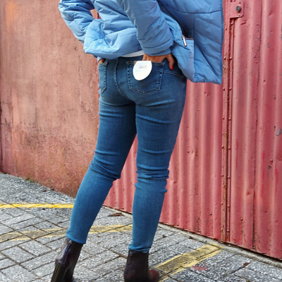 Pessoa a usar calças de ganga azuis justas com etiqueta 'BASIC', casaco acolchoado azul e botas pretas num cenário urbano.