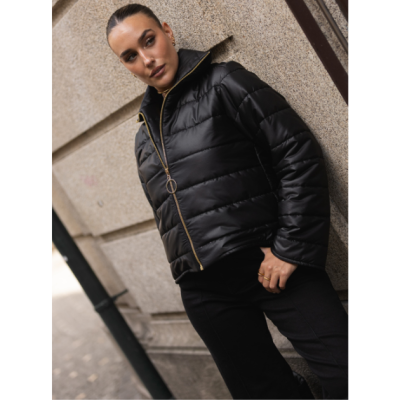 Casaco preto puff com fecho dourado e argola, mulher encostada em parede