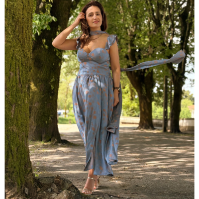 Vestido comprido azul claro com padrão castanho-avermelhado usado por mulher numa área arborizada