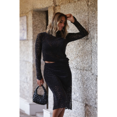Mulher com conjunto de renda preto e mala preta em parede de pedra cinzenta