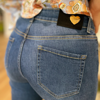 Calças jeans azuis com bolso traseiro e etiqueta preta com coração amarelo e texto, camisas florais laranja e bege