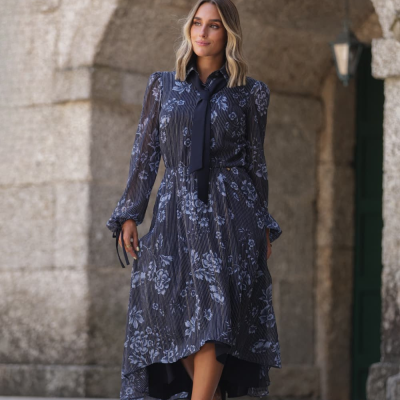 Vestido comprido preto com padrão floral cinza e riscas brancas, mangas transparentes, laço no pescoço e sapatos pretos de salto