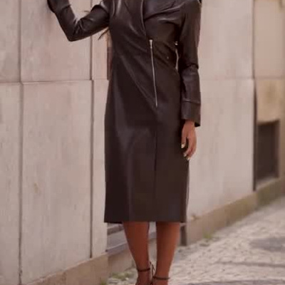 Mulher de vestido longo de couro preto e saltos altos num cenário urbano com texto miss YOU.