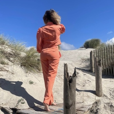 Mulher de costas com conjunto cor de salmão em ambiente de praia com areia e céu azul