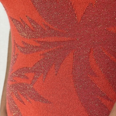 Tecido de roupa laranja com padrão de folhas e brilho dourado