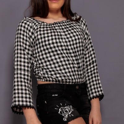 Jovem com blusa xadrez preta e branca e calções pretos com desenho de gato e texto