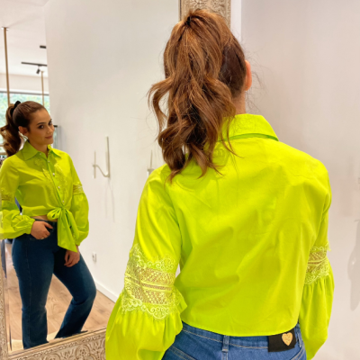 Camisa fluorescente verde com renda branca nas mangas e calças de ganga azuis, vista de costas perante espelho.