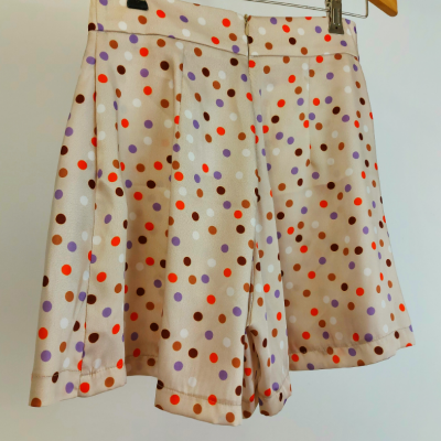 Calções bege com bolinhas coloridas num cabide de madeira