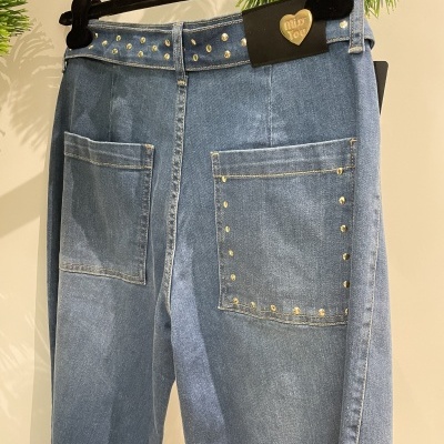 Calças de ganga azuis com bolsos grandes e tachas douradas penduradas num cabide preto