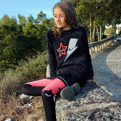 Criança vestindo camisola preta e leggings coloridas sentada em muro de pedra ao ar livre