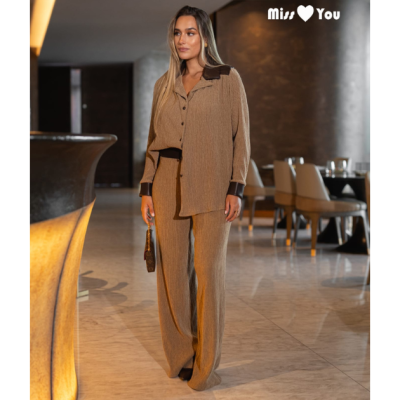 Conjunto feminino de camisa e calças castanhas claras com detalhes castanhos escuros usado por mulher em ambiente interior moderno