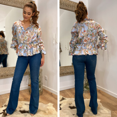 Blusa floral com folhos e calças de ganga azul em modelo mulher em sala com espelho