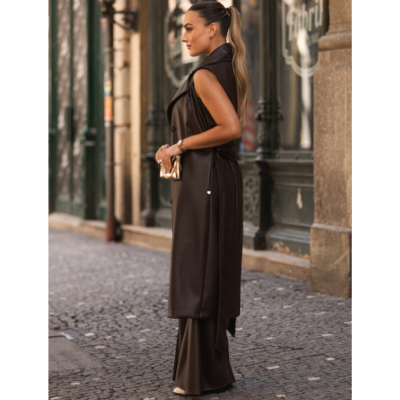 Mulher de perfil com colete longo preto de couro sintético e calças largas na rua