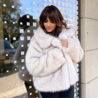 Mulher usando casaco de pele sintética creme contra fundo de vidro com pequenos quadrados