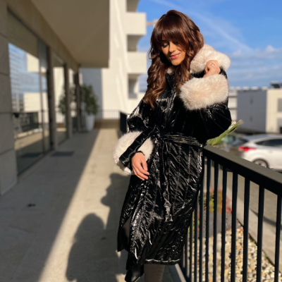 Mulher com casaco comprido preto brilhante com detalhes em pelo branco na varanda