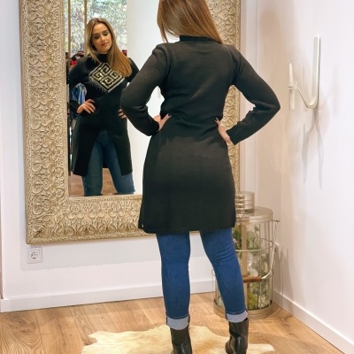 Mulher com casaco preto e jeans azuis em frente a espelho com moldura decorada