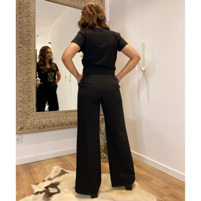 Mulher de costas com roupa preta e salto alto em frente a espelho com moldura decorativa.