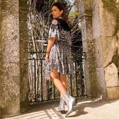 Vestido animal print preto e branco com botas prateadas, mulher de costas, arco de pedra ao fundo