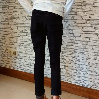 Calças pretas justas vistas de trás em ambiente interior com parede de pedra.