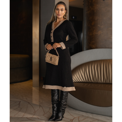 Mulher com vestido midi cinza escuro com detalhes bege, botas pretas altas e mala bege pequena