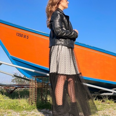 Mulher vestida com jaqueta preta e vestido com saia de tule preta ao lado de barco laranja e azul