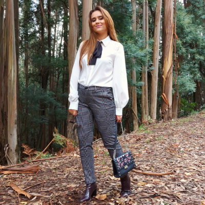 Mulher vestida com camisa branca, calças xadrez e botas pretas em floresta