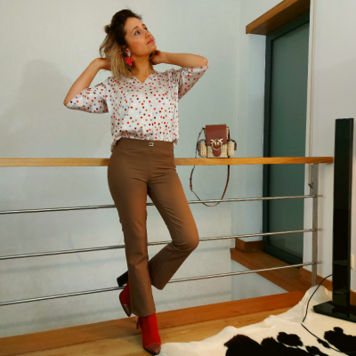 Mulher com camisa estampada e calças marrons apoiada em corrimão interior