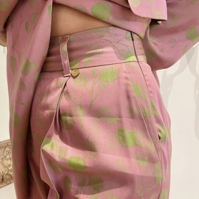 Calças rosas com padrão floral verde claro e botões dourados.