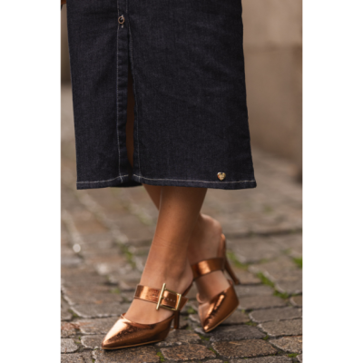 Sapatos bronze metálicos de salto com fivela dourada e saia ou calças de ganga escuras em calçada de pedra