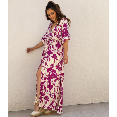 Vestido comprido feminino rosa com padrão floral junto a parede clara.