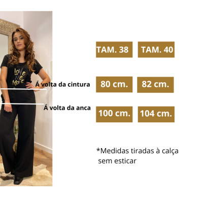 Mulher com calças pretas largas e camisa preta com texto dourado em interior com espelho