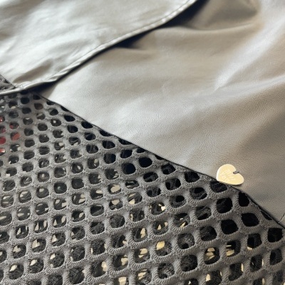 Peça de couro cinza claro sobre tecido preto com malha hexagonal e ícone dourado em forma de coração.