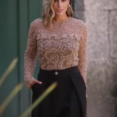 Modelo feminina com blusa rendada bege e calças pretas a desfilar ao ar livre