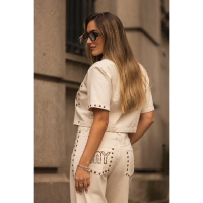 Mulher de costas a usar conjunto bege com tachas metálicas formando a palavra MY no bolso