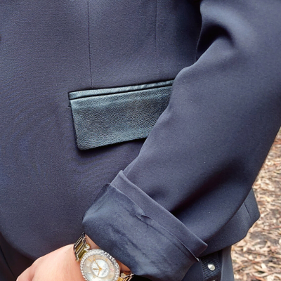 Blazer azul escuro com bolso preto texturizado e punho dobrado, com relógio dourado no pulso