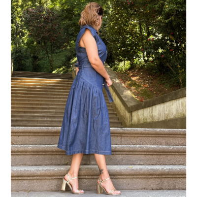Vestido azul midi com cinto e sandálias douradas, modelo está numa escadaria exterior com árvores ao redor.