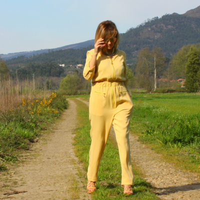 Mulher com macacão amarelo caminhando numa estrada de terra em área rural