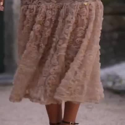 Mulher a usar vestido longo nude com padrão floral e sapatos de salto alto castanhos.
