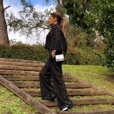 Mulher com roupa preta rendada e mala prateada em ambiente exterior