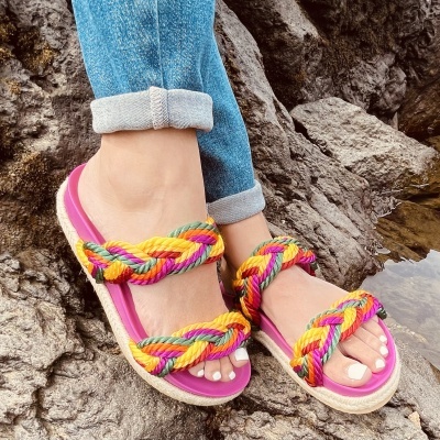 Sandálias trançadas coloridas com sola rosa usadas em pedras