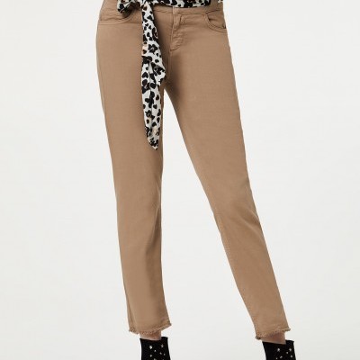 Calças bege justas com bainha desfiada, botas pretas com tachas, blusa estampada com padrão animal e laço