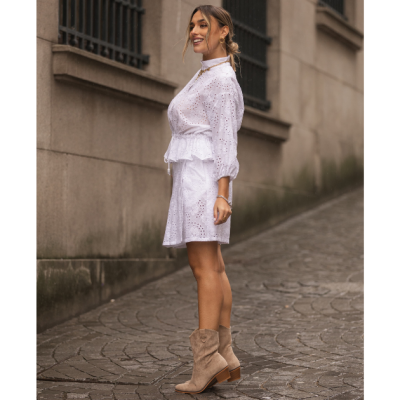 Mulher de vestido branco bordado e botas bege a andar num passeio de pedra