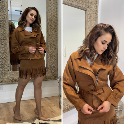 Mulher com conjunto castanho em camurça e sapatos nude junto a espelho decorativo